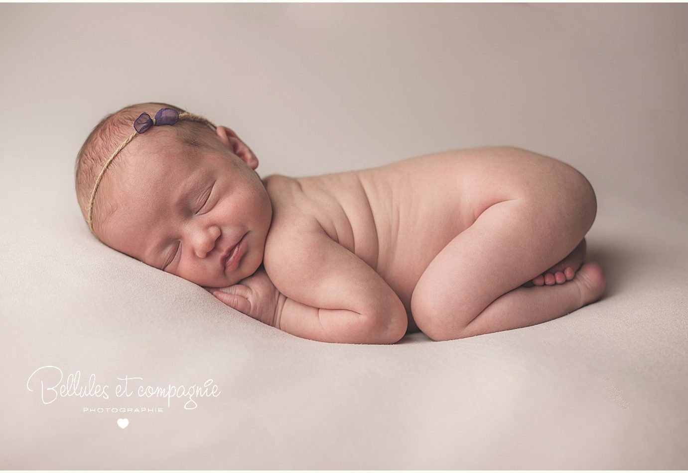 Bébé nouveau-né sur fond rose pâle en séance newborn posing par le studio Bellules et Compagnie à Clermont-Ferrand