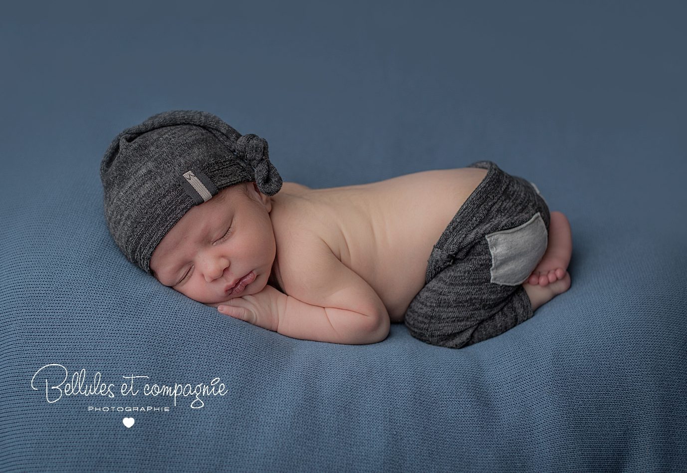 Nouveau-né sur fond bleu avec petit bonnet et pantalon par Bellules et Compagnie photographe près de Clermont-Ferrand