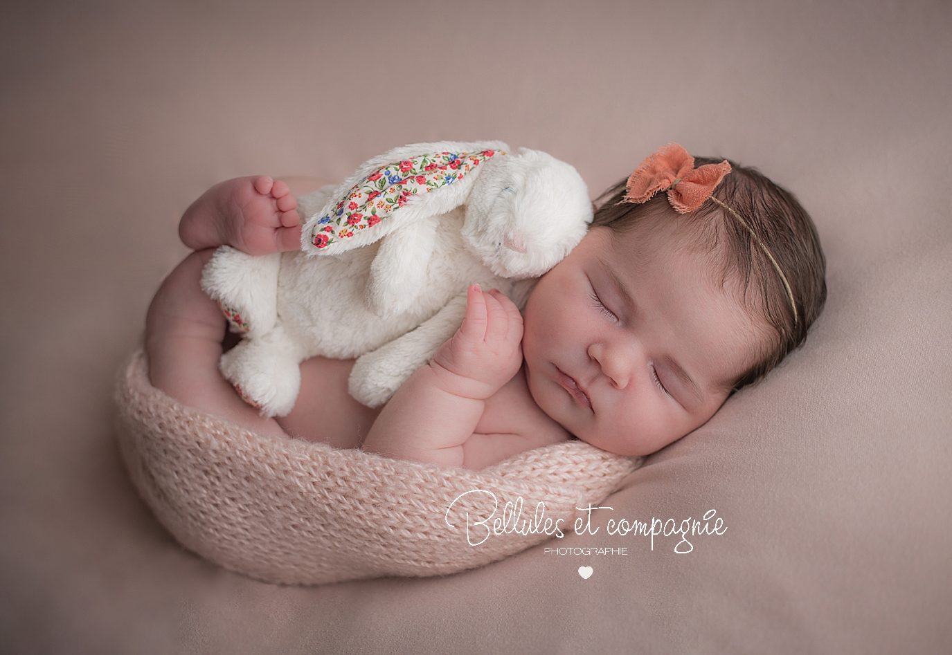 Bébé sur fond rose pâle et peluche lapin blanc en séance nouveau-né par photographe Bellules et Compagnie dans le Puy-de-Dôme