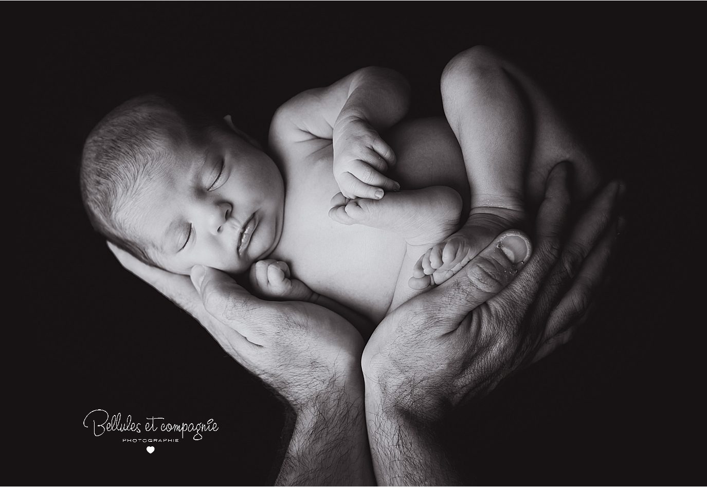 Nouveau-né dans main de papa en noir et blanc en séance newborn posing par Bellules et Compagnie photographe Clermont-Ferrand