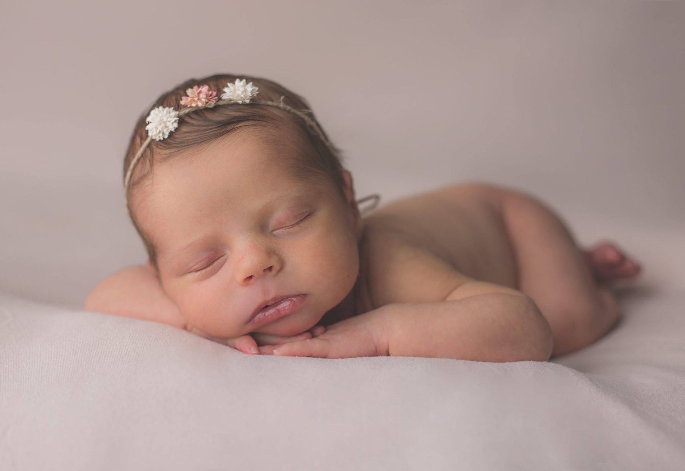 Petit bébé sur fond rose avec mains sous le menton en séance naissance par photographe Bellules et Compagnie à Clermont-Ferrand